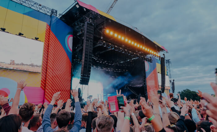 People Raising their hands energetically on a Music Festival in front of a stage.